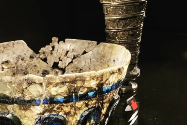 Glasskål i förgrunden med många sprickor och metallbägare i bakgrunden.