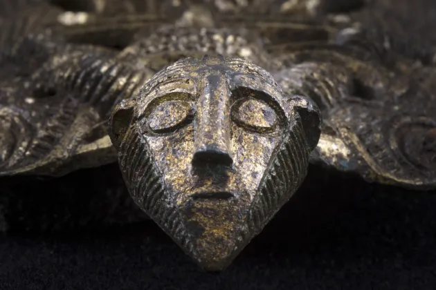 En metallfigur som föreställer en bevingad man. Vingarna har snirkliga mönster.