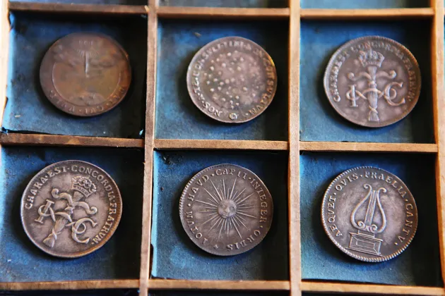 Sex stycken historiska mynt med bronsfärg ligger i två rader i små fack med turkos, sliten tygbakgrund