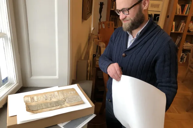 Foto på man som står och tittar på medeltida pappersmaterial.