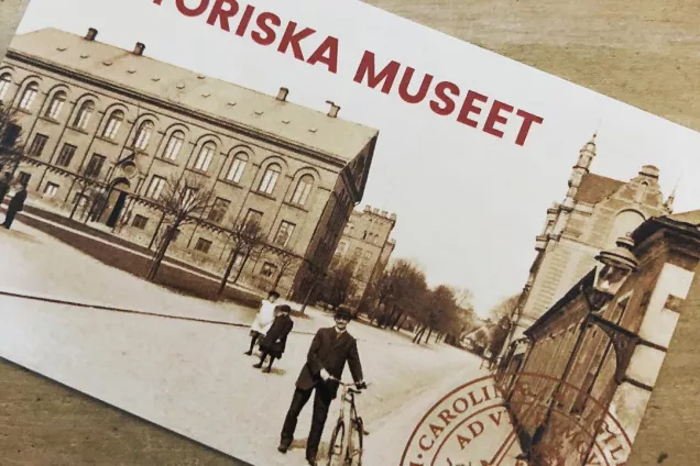 Ett papperskort med svartvit bild på museet. Framför står en man i hatt med sin cykel.