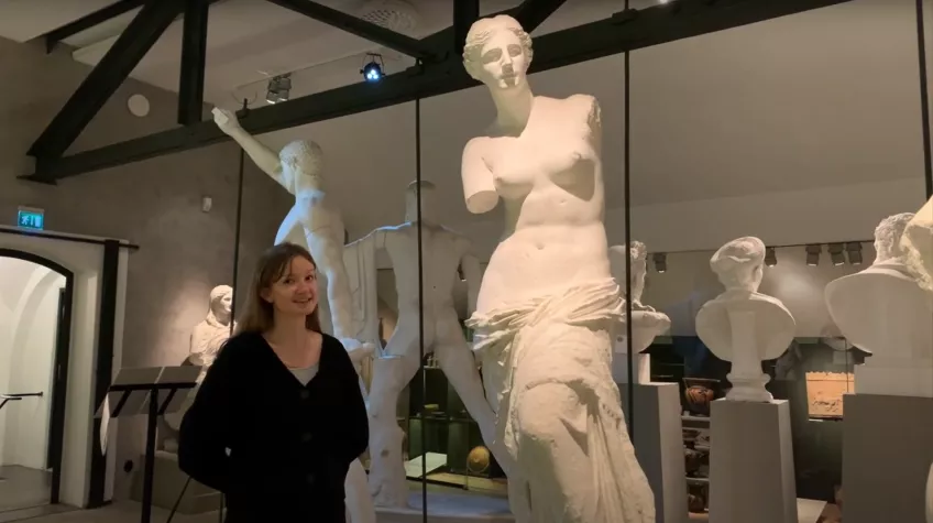 Svartklädd kvinna står i en sal med vita antika skulpturer.
